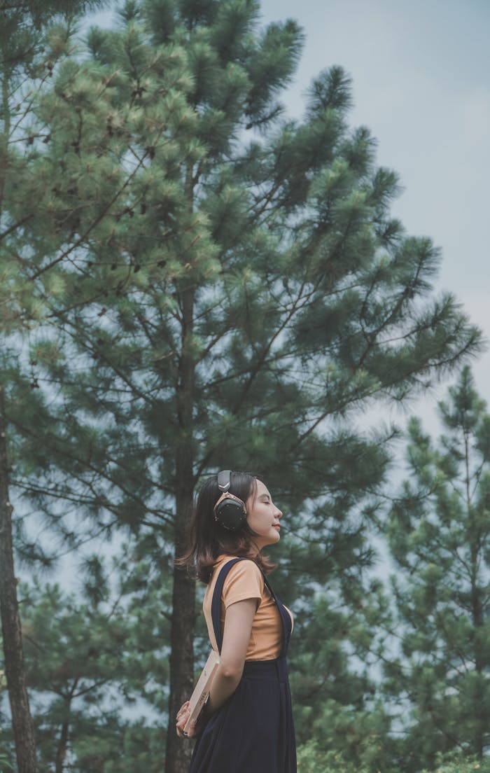 Woman with headphones enjoying nature and music in a tranquil forest setting.